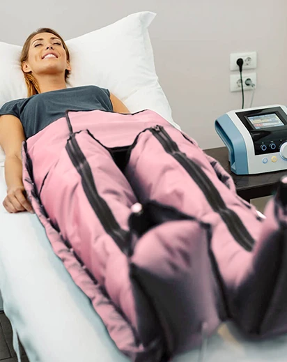 Mujer sonriendo y relajada en una camilla de Paola Zampetti Estética, recibiendo un tratamiento de presoterapia corporal avanzado con el traje de compresión de piernas color rosa aplicado para drenaje linfático y celulitis.