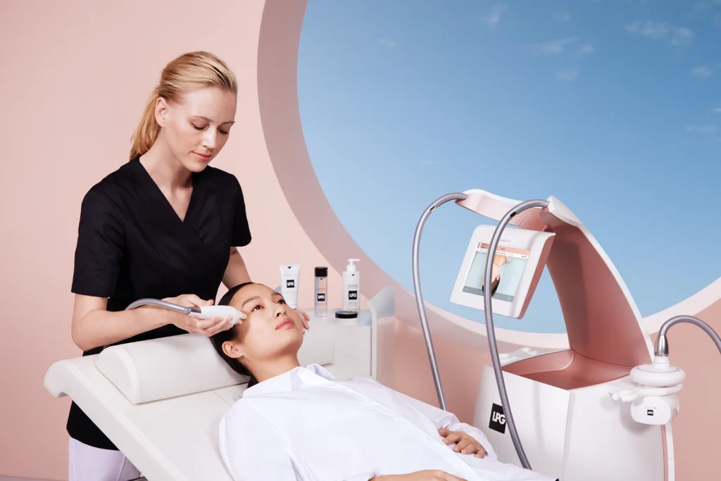 Profesional de estética aplicando un tratamiento facial con el cabezal del equipo LPG Alliance a una paciente que descansa relajada en una camilla clínica.